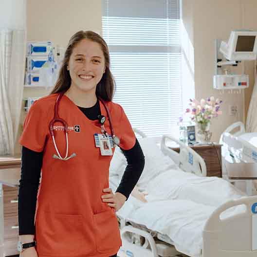 A nursing student poses for a photo in the nursing lab